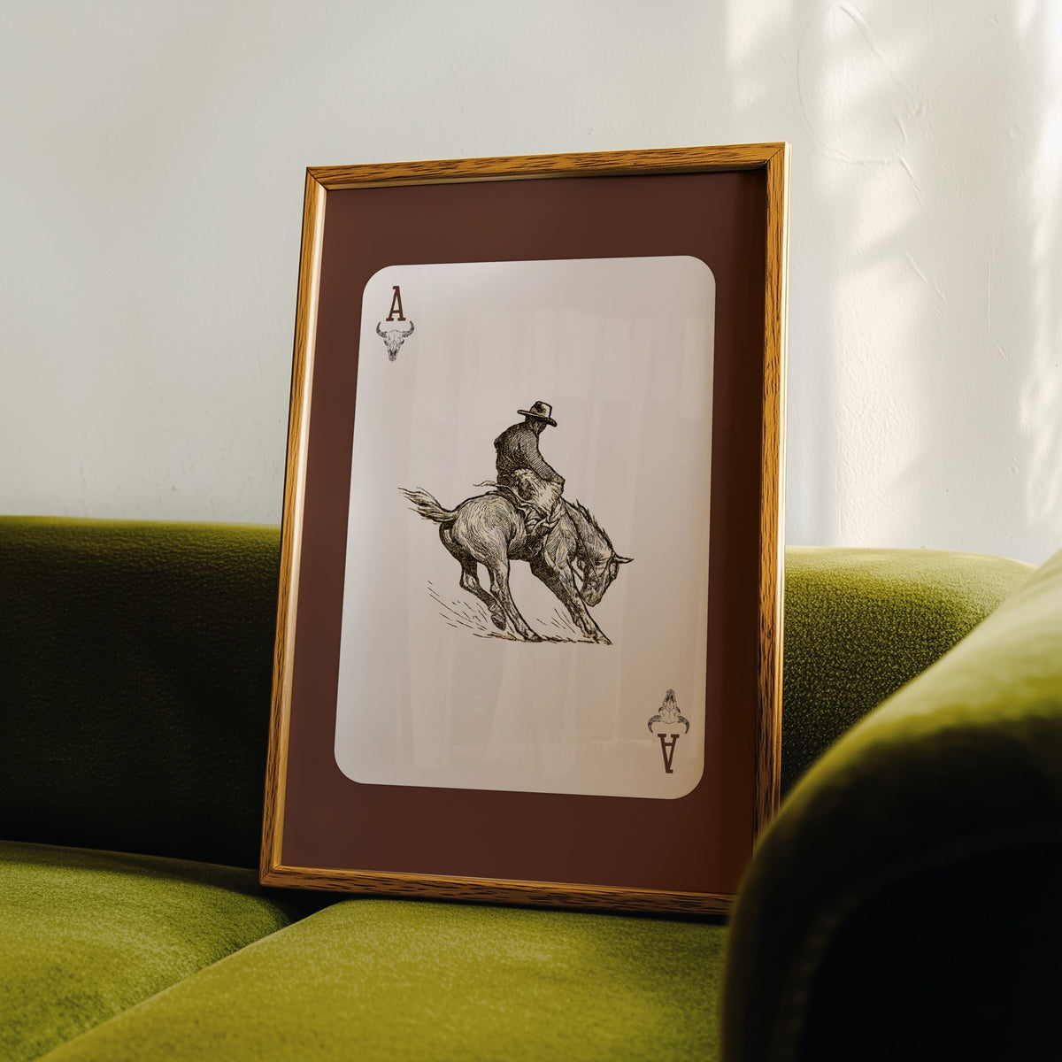 Bronco rider ace card print in an oak frame leaning on a green velvet sofa