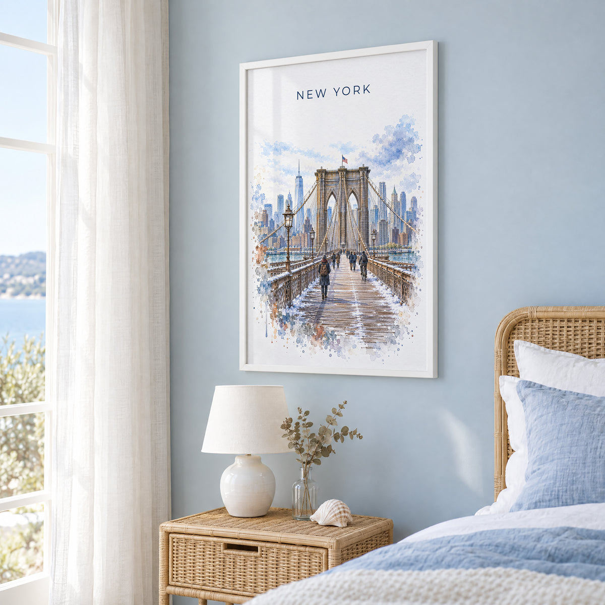 Brooklyn Bridge watercolor print in a white frame on a pale blue wall beside a rattan bed in a coastal bedroom