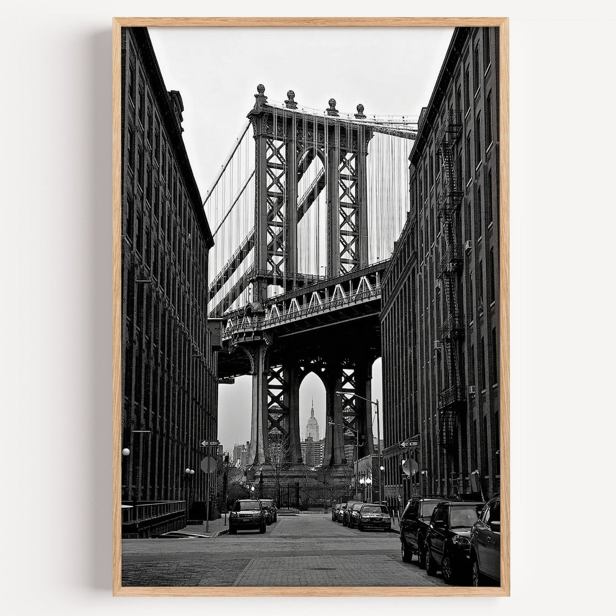 Manhattan Bridge between brick buildings print in a light oak frame on a plain white wall