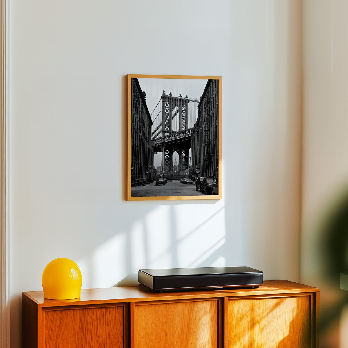 Manhattan Bridge between brick buildings print in an oak frame above a teak sideboard with a yellow glass lamp
