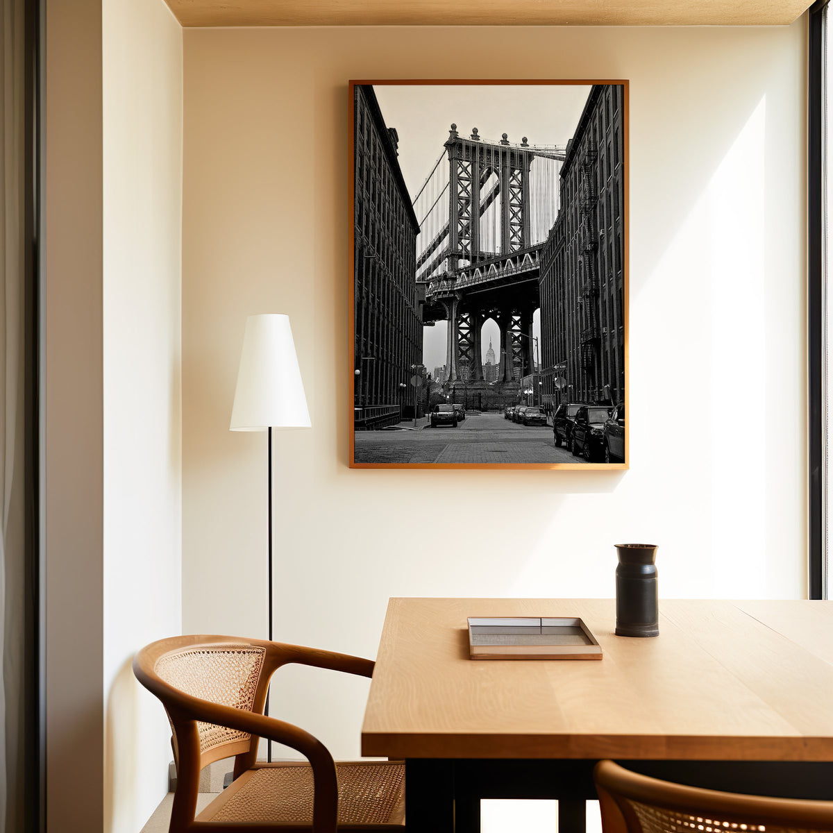 Manhattan Bridge between brick buildings print in an oak frame above a dining table and cane chair