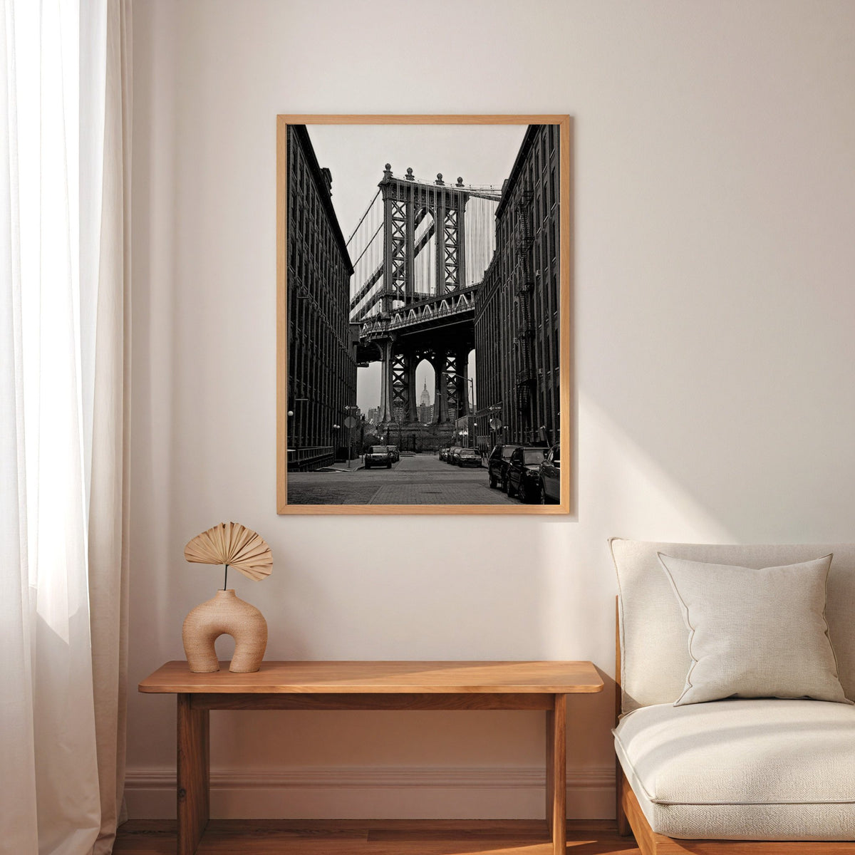 Manhattan Bridge between brick buildings print in an oak frame above a narrow console with an arched vase