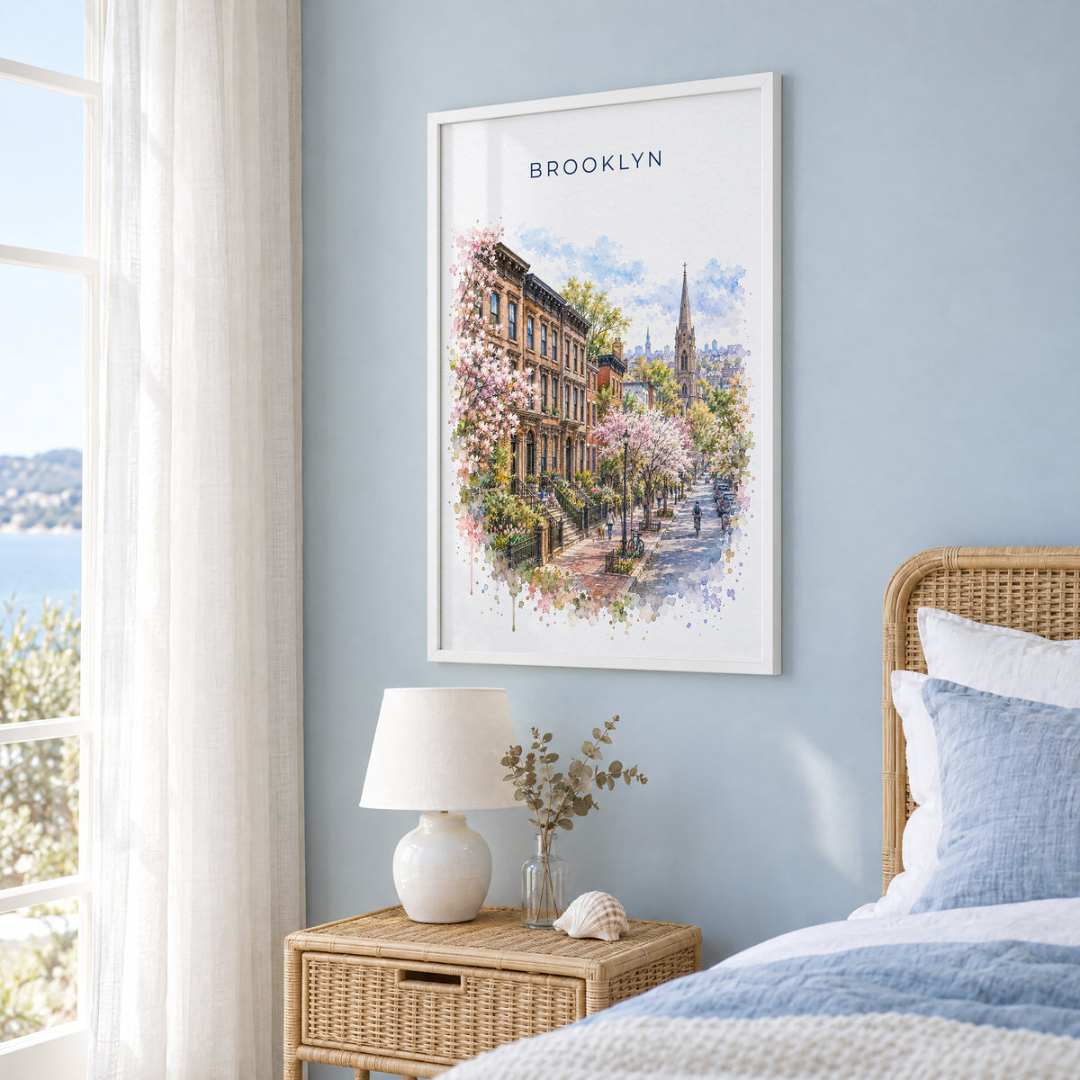 Brooklyn watercolor print in a white frame on a pale blue wall beside a rattan bed in a coastal bedroom