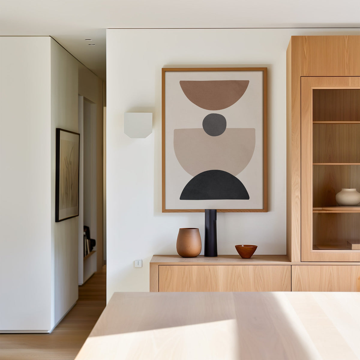 Brown bowl and black arch stacked shapes print in an oak frame above a light oak sideboard in a dining room