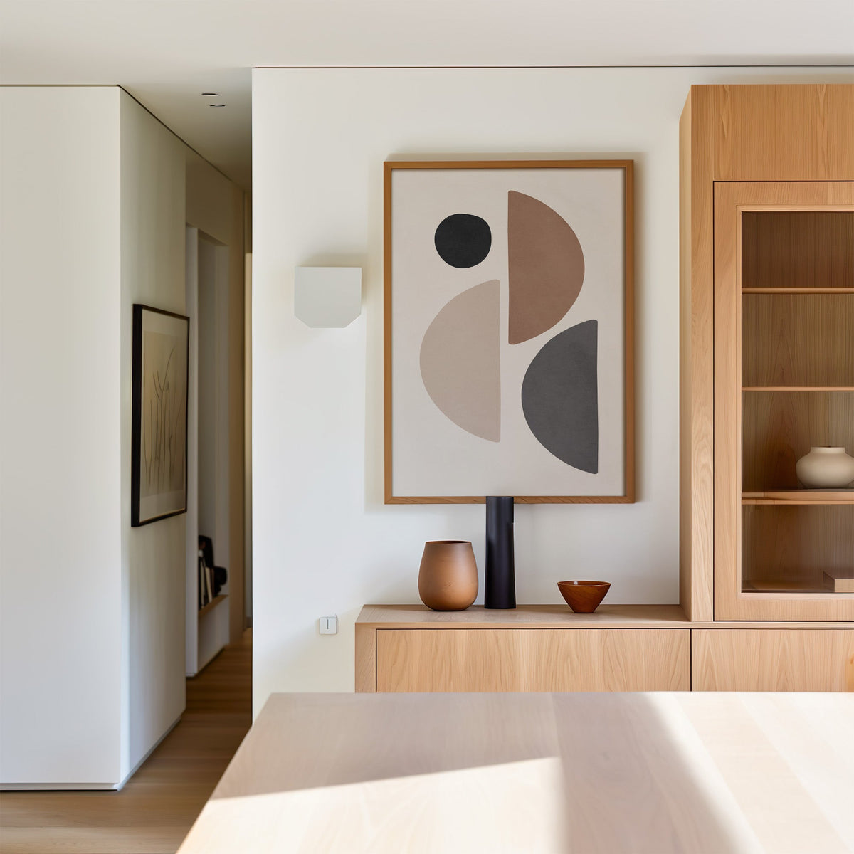 Brown, grey and black split circle shapes print in an oak frame above a light oak sideboard in a dining room