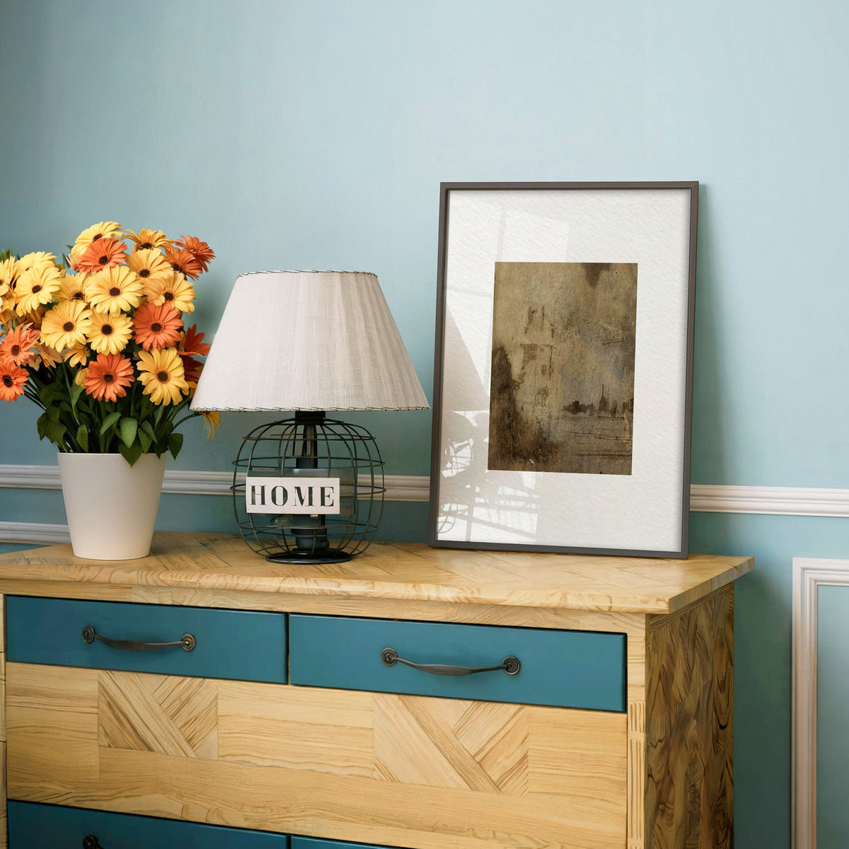 Brown wash ghost tower and waterline print in a charcoal frame on a teal dresser beside orange and yellow daisies