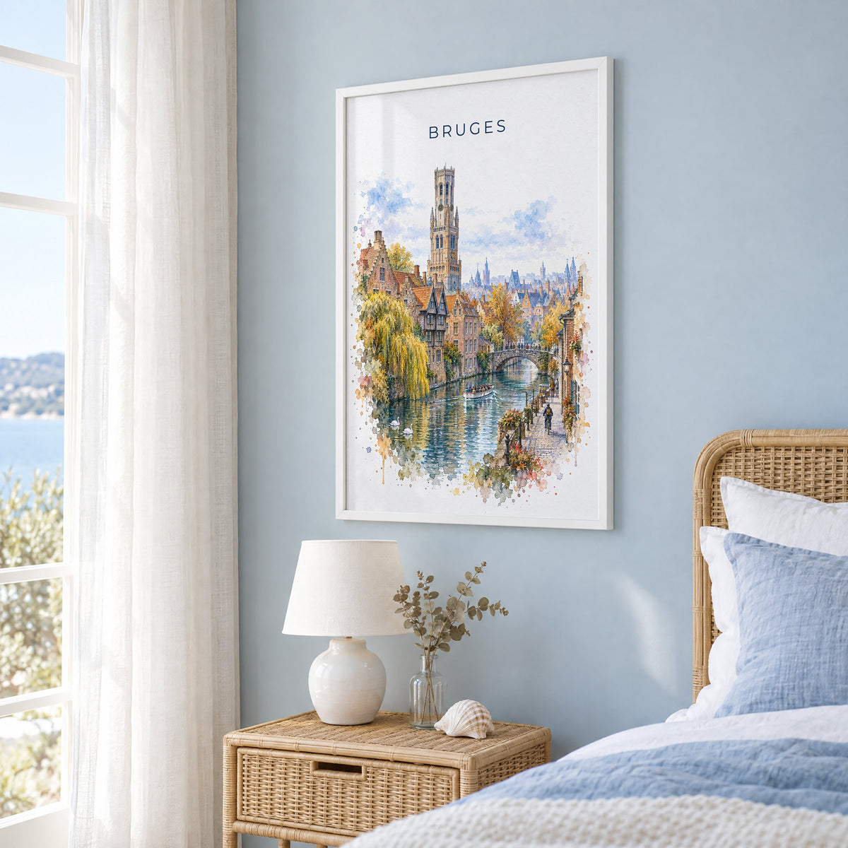 Bruges watercolor print in a white frame on a pale blue wall beside a rattan bed in a coastal bedroom