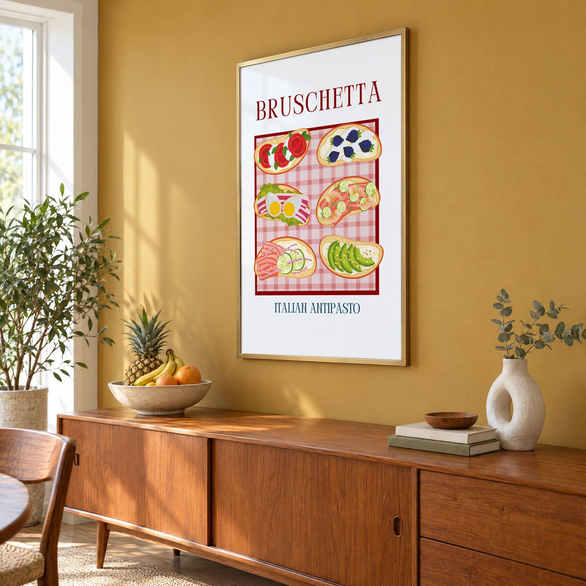 BRUSCHETTA six toasts pink gingham print in a brass frame on a mustard wall above a teak sideboard with a fruit bowl, seen at an angle