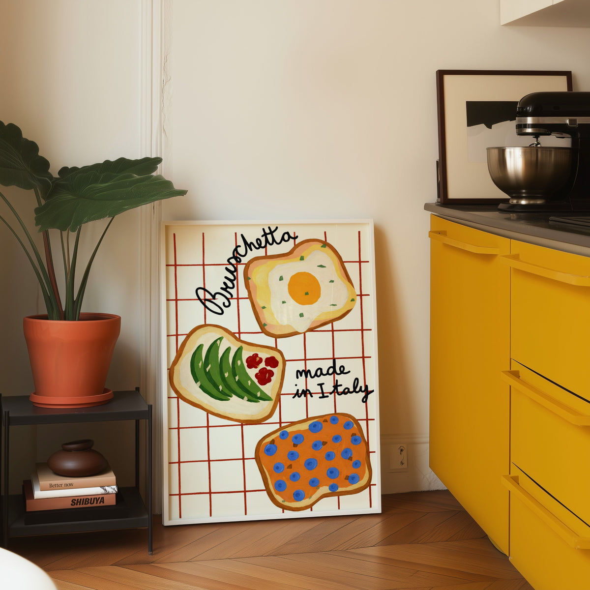 Bruschetta print in a white frame leaning on parquet beside a bright yellow kitchen