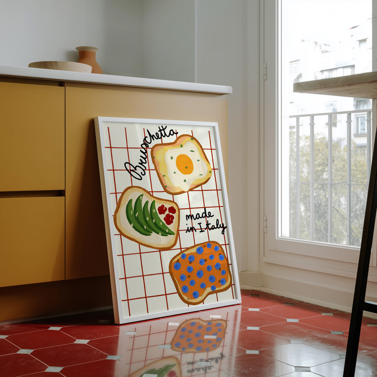 Bruschetta print in a white frame against butter yellow cabinets on a red tiled floor