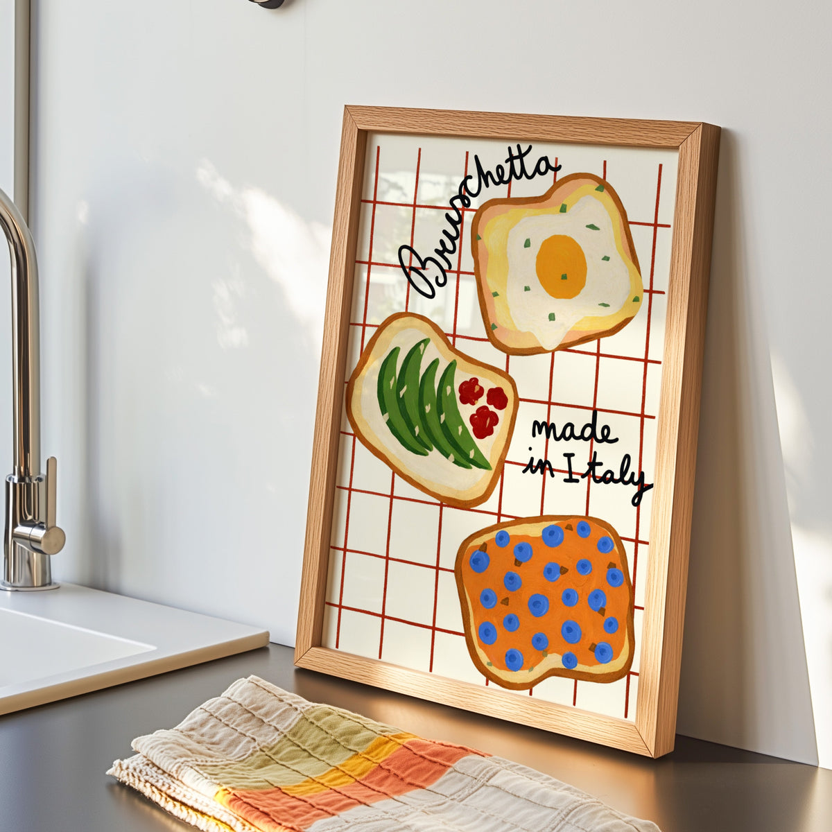Bruschetta print in an oak frame leaning by the kitchen sink beside a striped tea towel