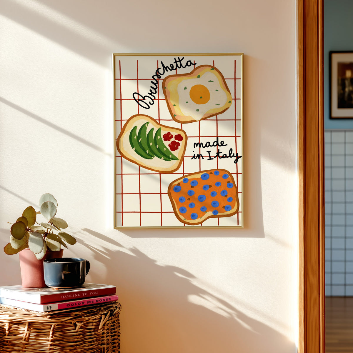 Bruschetta print in a gold frame above a basket of books and a pilea plant