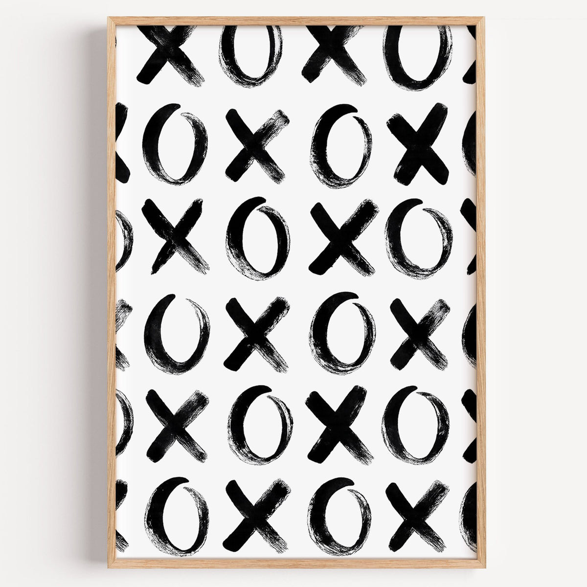 Hand-brushed XOXO pattern print in a light oak frame on a plain white wall