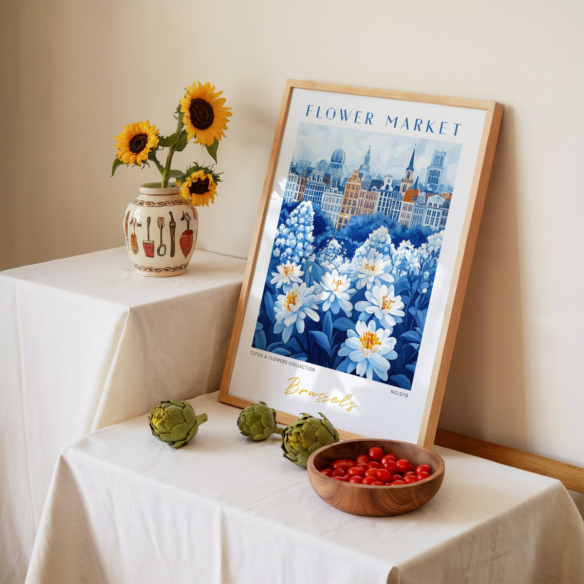 Brussels flower market print in an oak frame leaning on a linen-draped table beside a vase of sunflowers