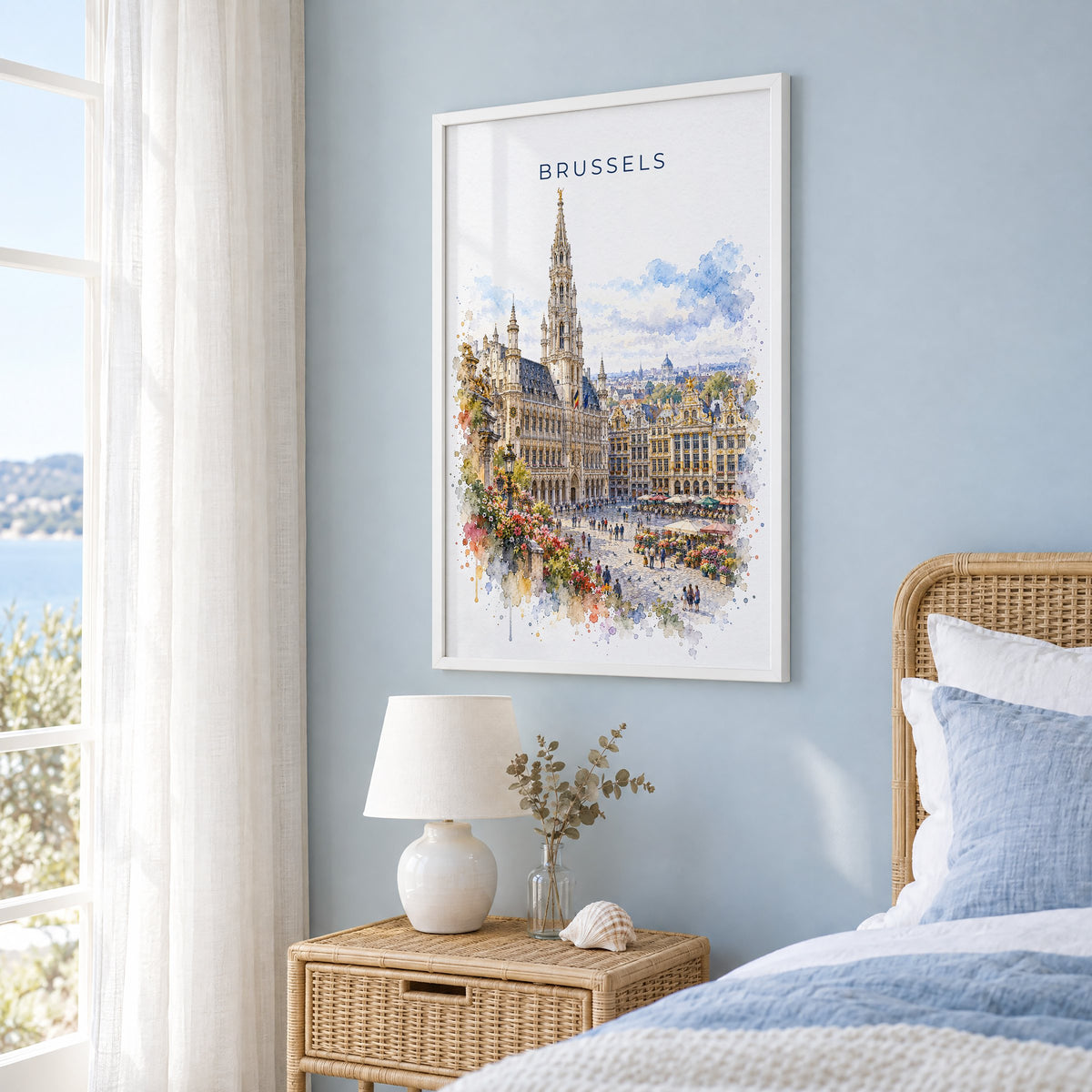 Brussels watercolor print in a white frame on a pale blue wall beside a rattan bed in a coastal bedroom