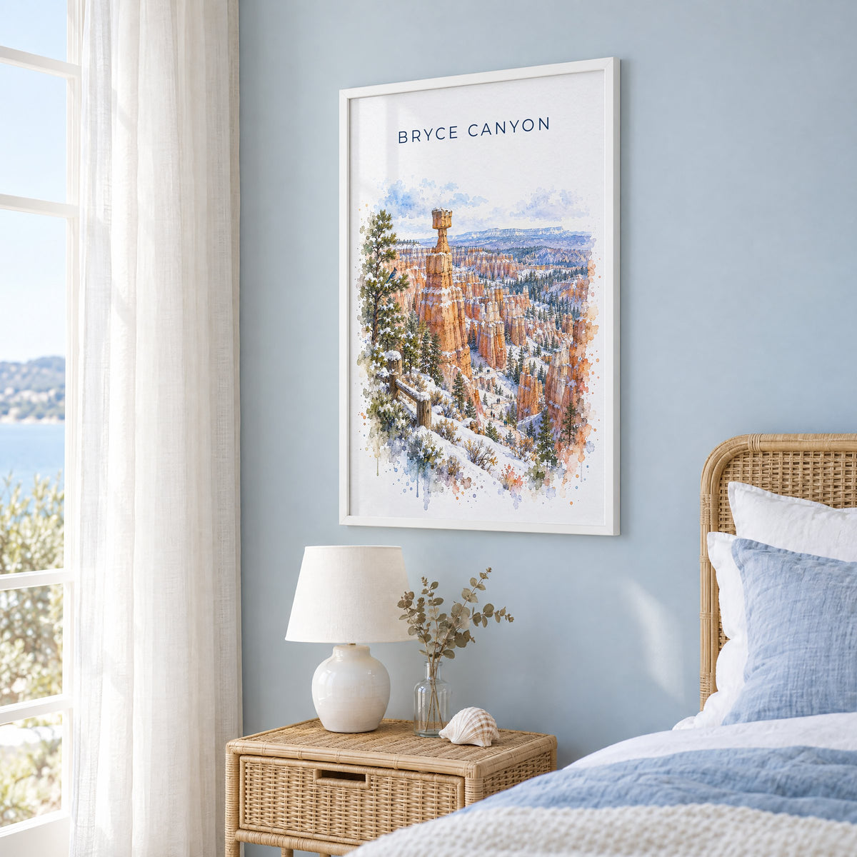 Bryce Canyon National Park watercolor print in a white frame on a pale blue wall beside a rattan bed in a coastal bedroom