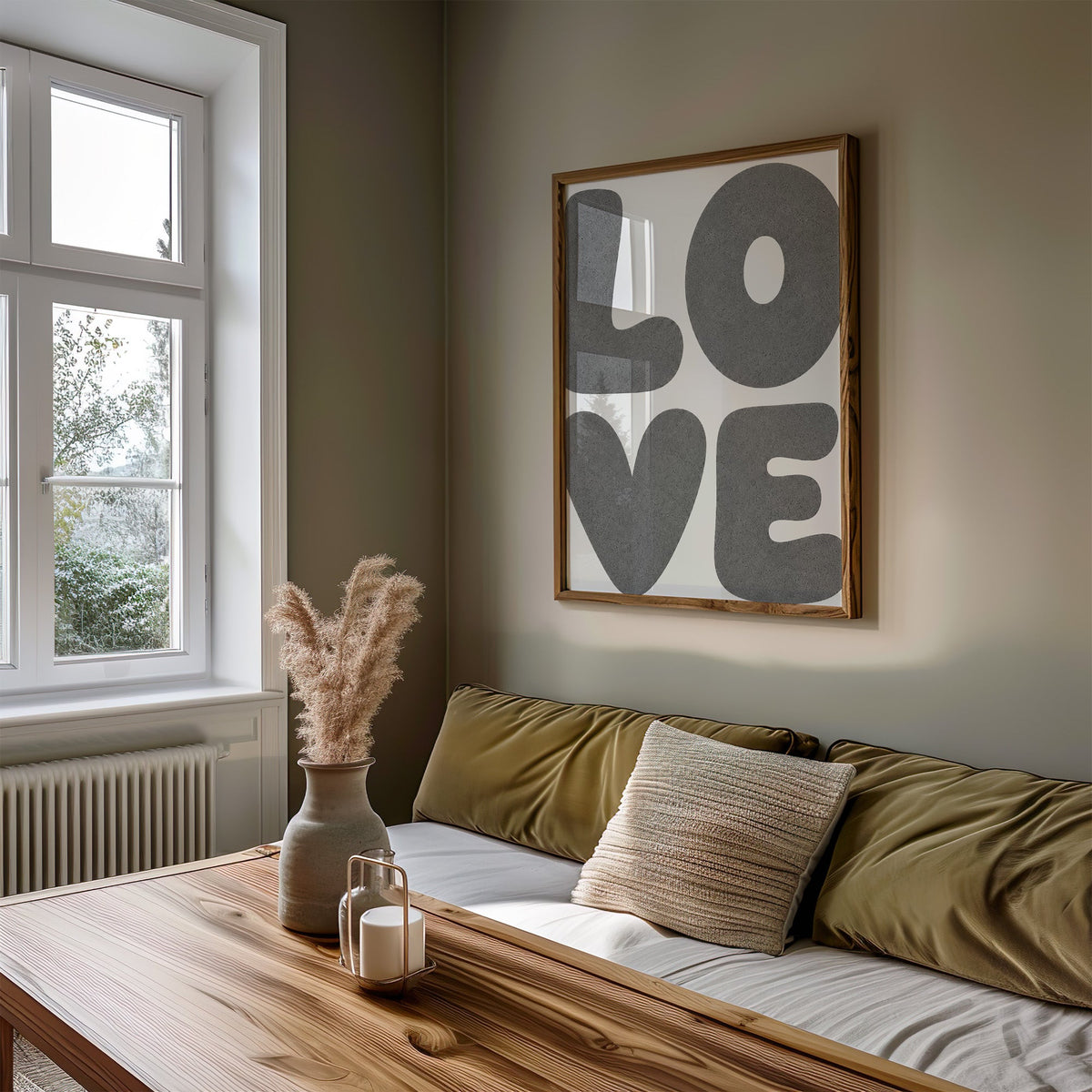 Giant grey bubble letters spelling love print in a walnut frame above an olive daybed by a window