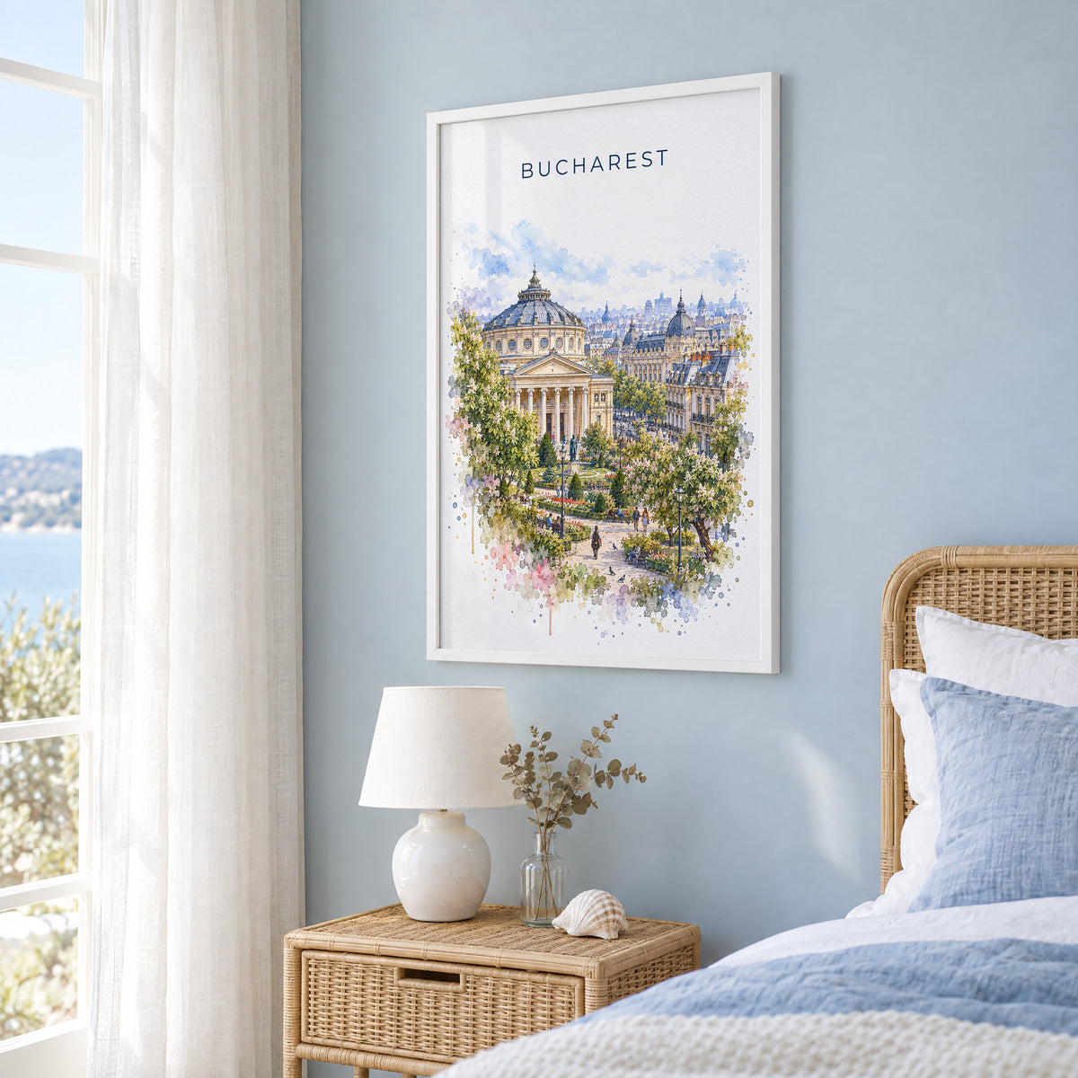 Bucharest watercolor print in a white frame on a pale blue wall beside a rattan bed in a coastal bedroom