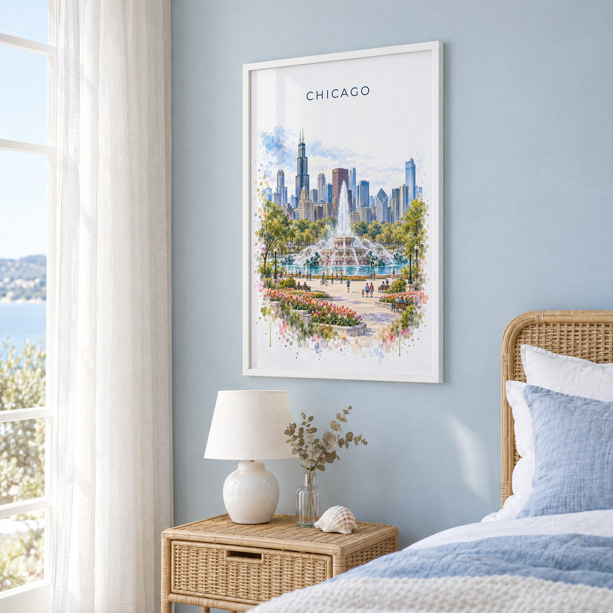 Buckingham Fountain Chicago watercolor print in a white frame on a pale blue wall beside a rattan bed in a coastal bedroom