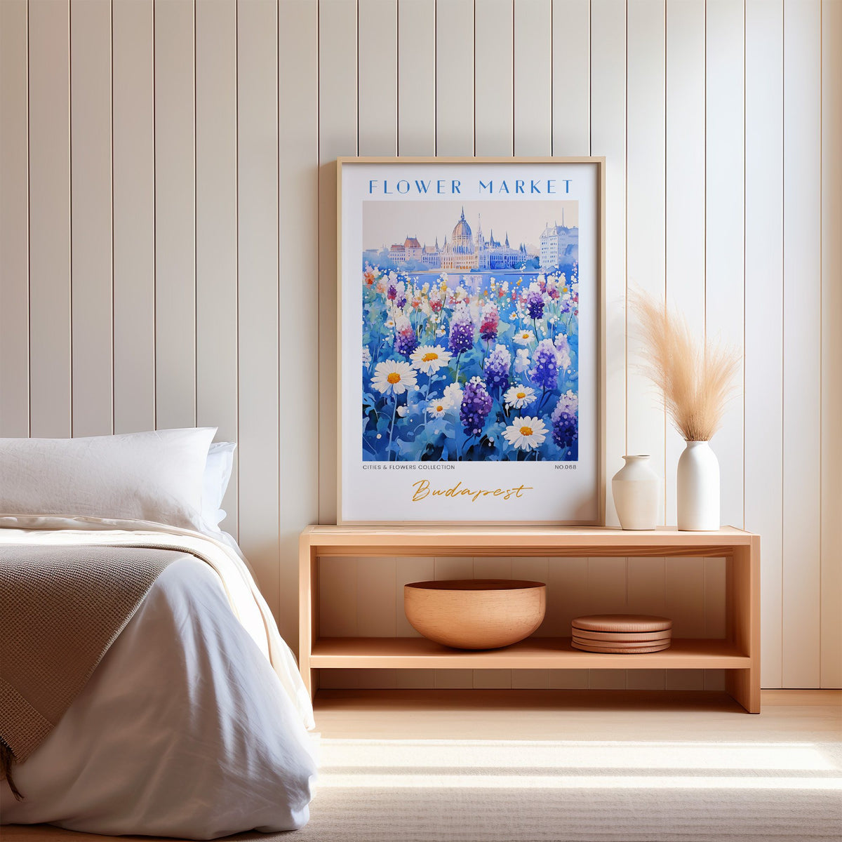 Budapest flower market print in an oak frame on a wood bench against a white shiplap bedroom wall with pampas grass