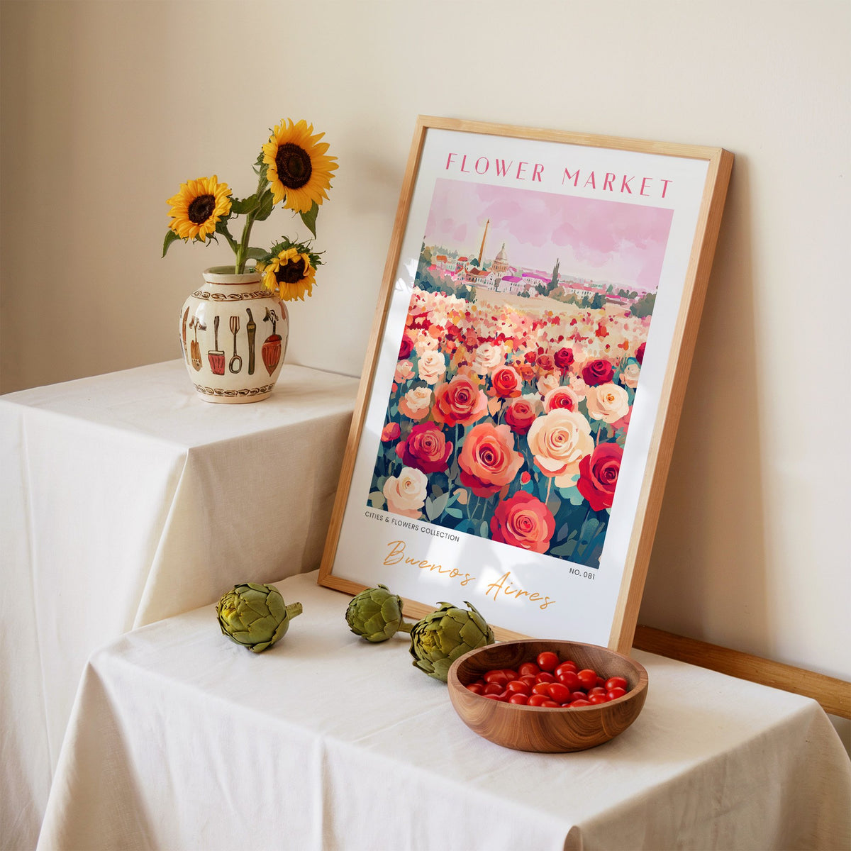 Buenos Aires flower market print in an oak frame leaning on a linen-draped table beside a vase of sunflowers