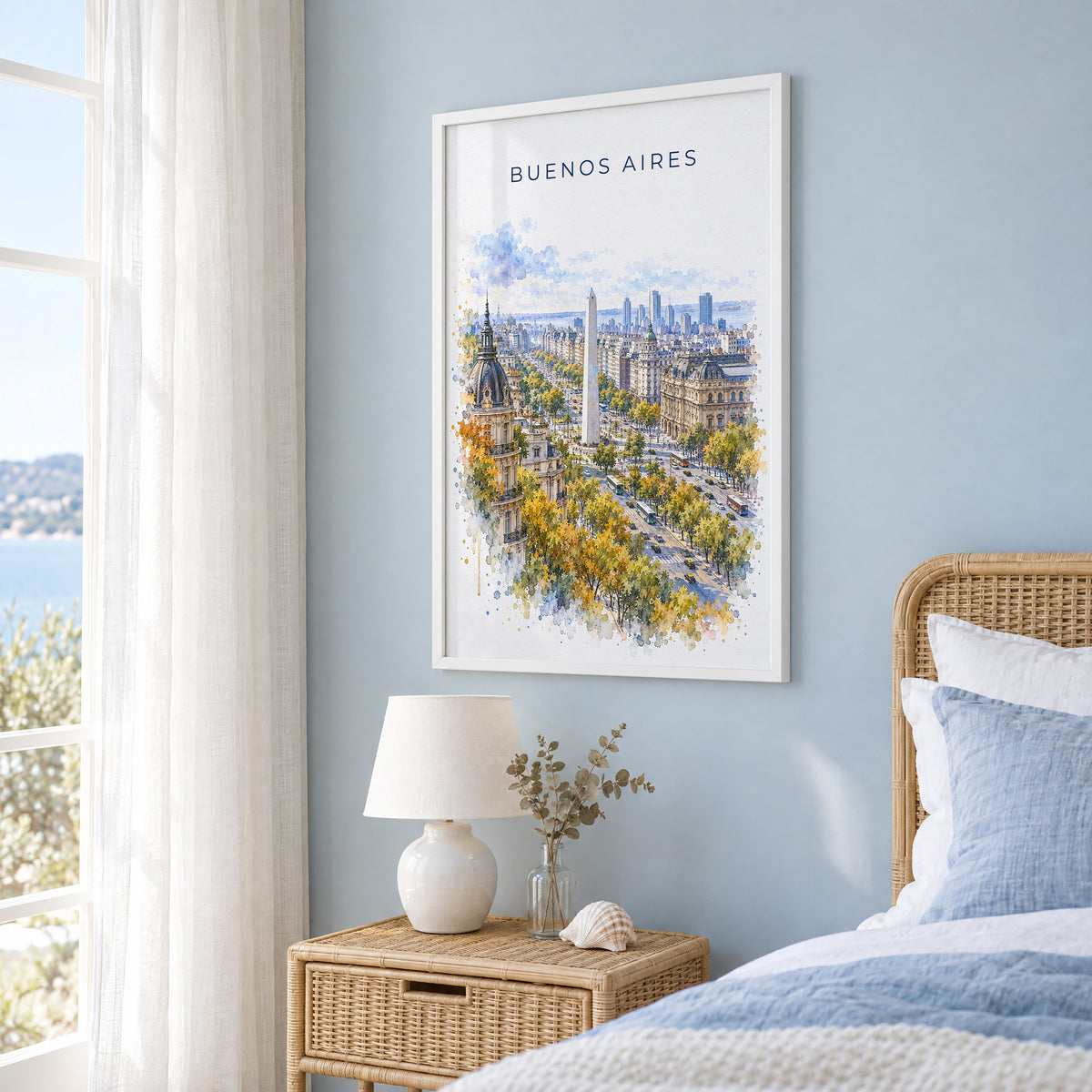 Buenos Aires watercolor print in a white frame on a pale blue wall beside a rattan bed in a coastal bedroom