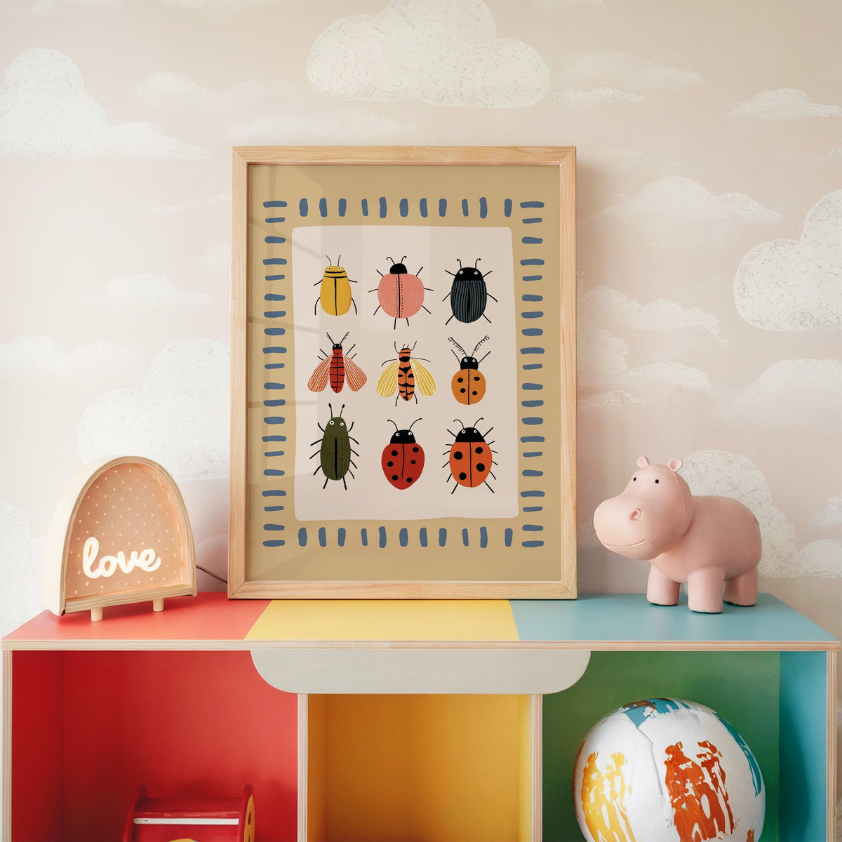Bug collection chart nursery print in an oak frame on a rainbow toy shelf against cloud wallpaper
