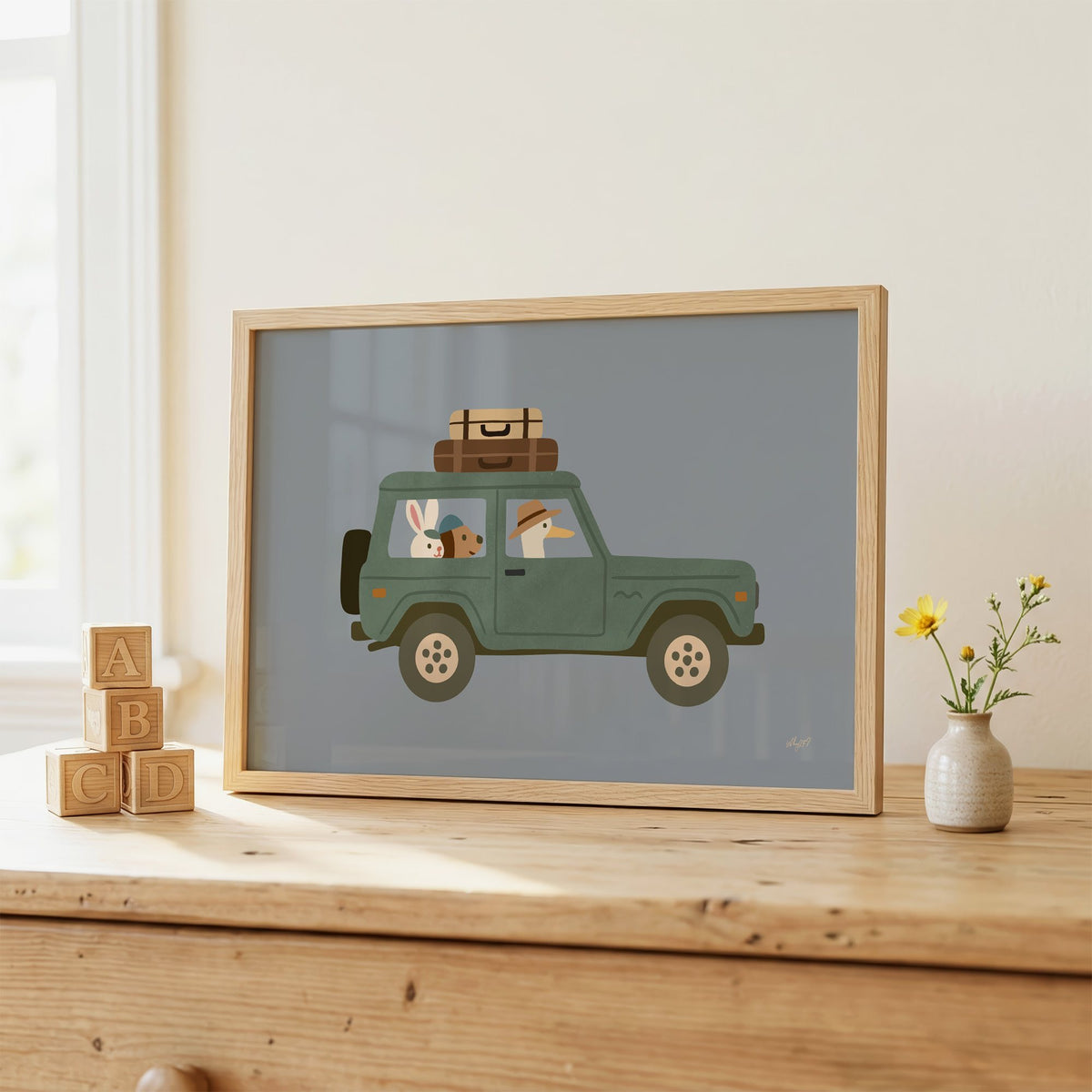 Animals riding green vintage suv nursery print in an oak frame on a wooden dresser beside ABC blocks