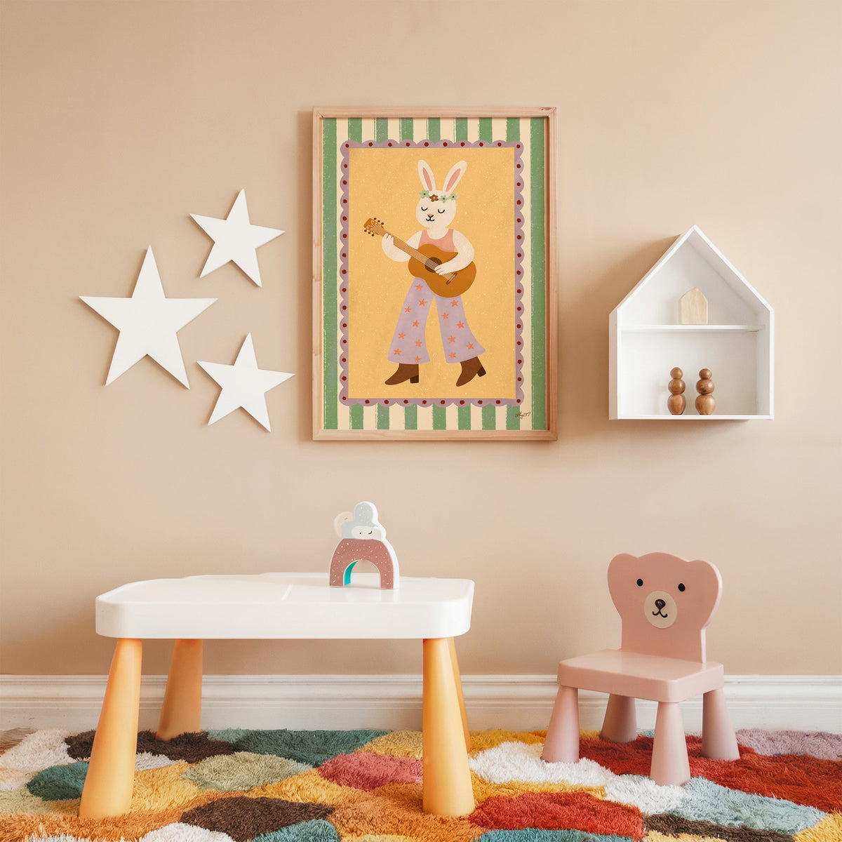 Bunny playing guitar with flower crown nursery print in an oak frame on a peach wall above a kids table with wall stars
