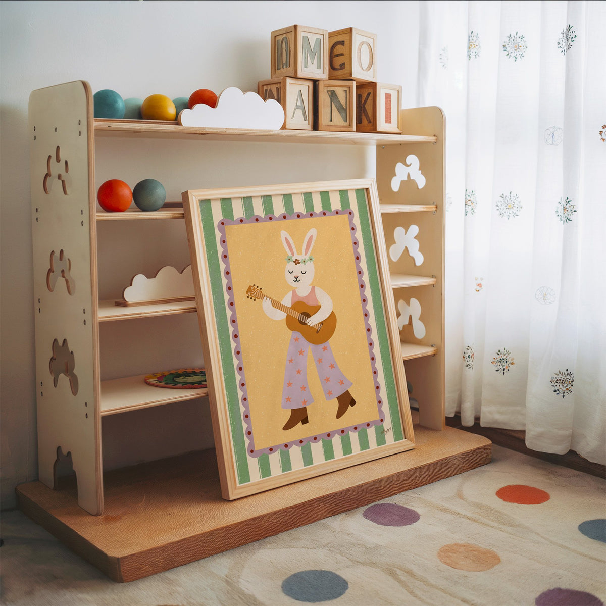 Bunny playing guitar with flower crown nursery print in an oak frame leaning on a toy shelf with wooden letter blocks