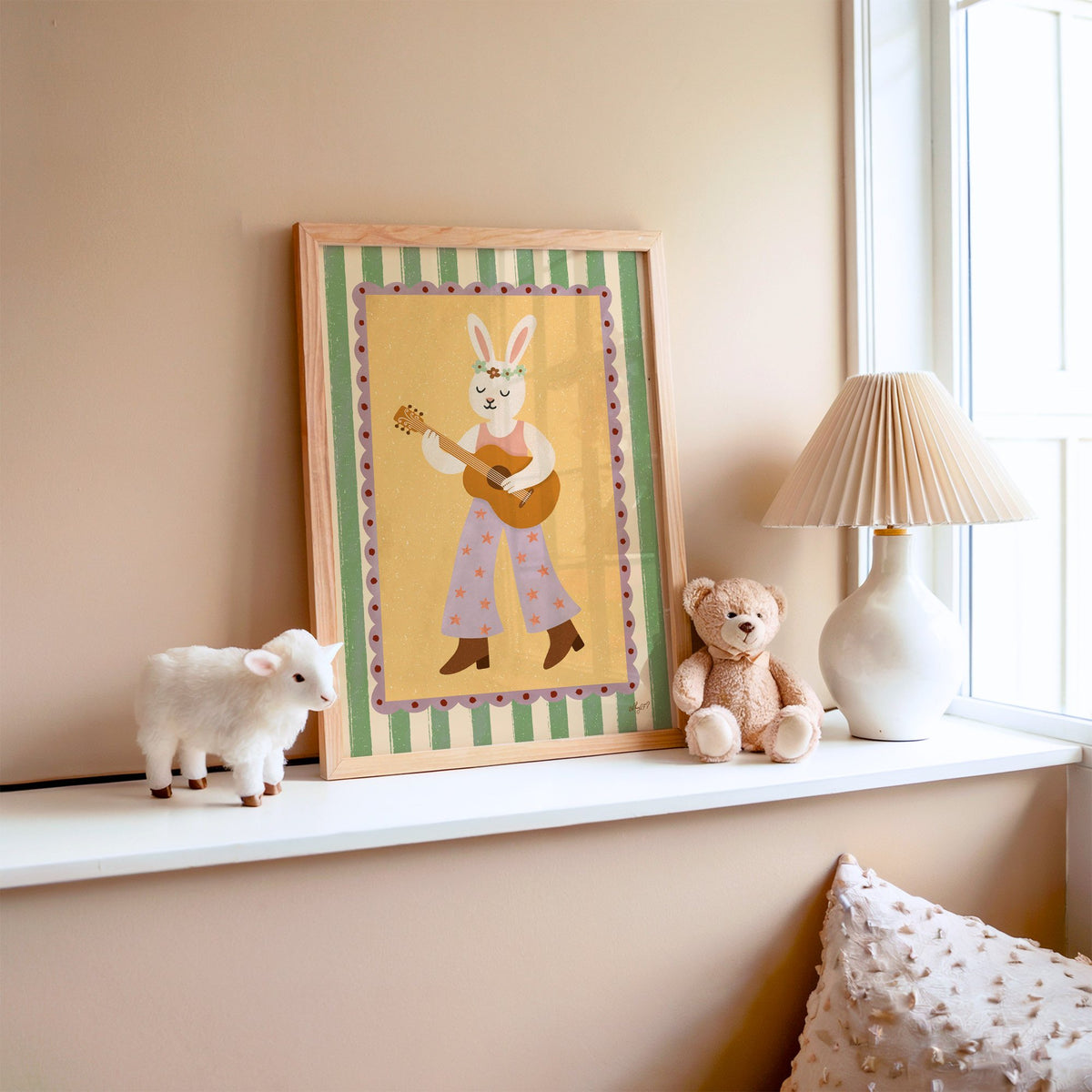 Bunny playing guitar with flower crown nursery print in an oak frame on a window ledge with a toy lamb and teddy