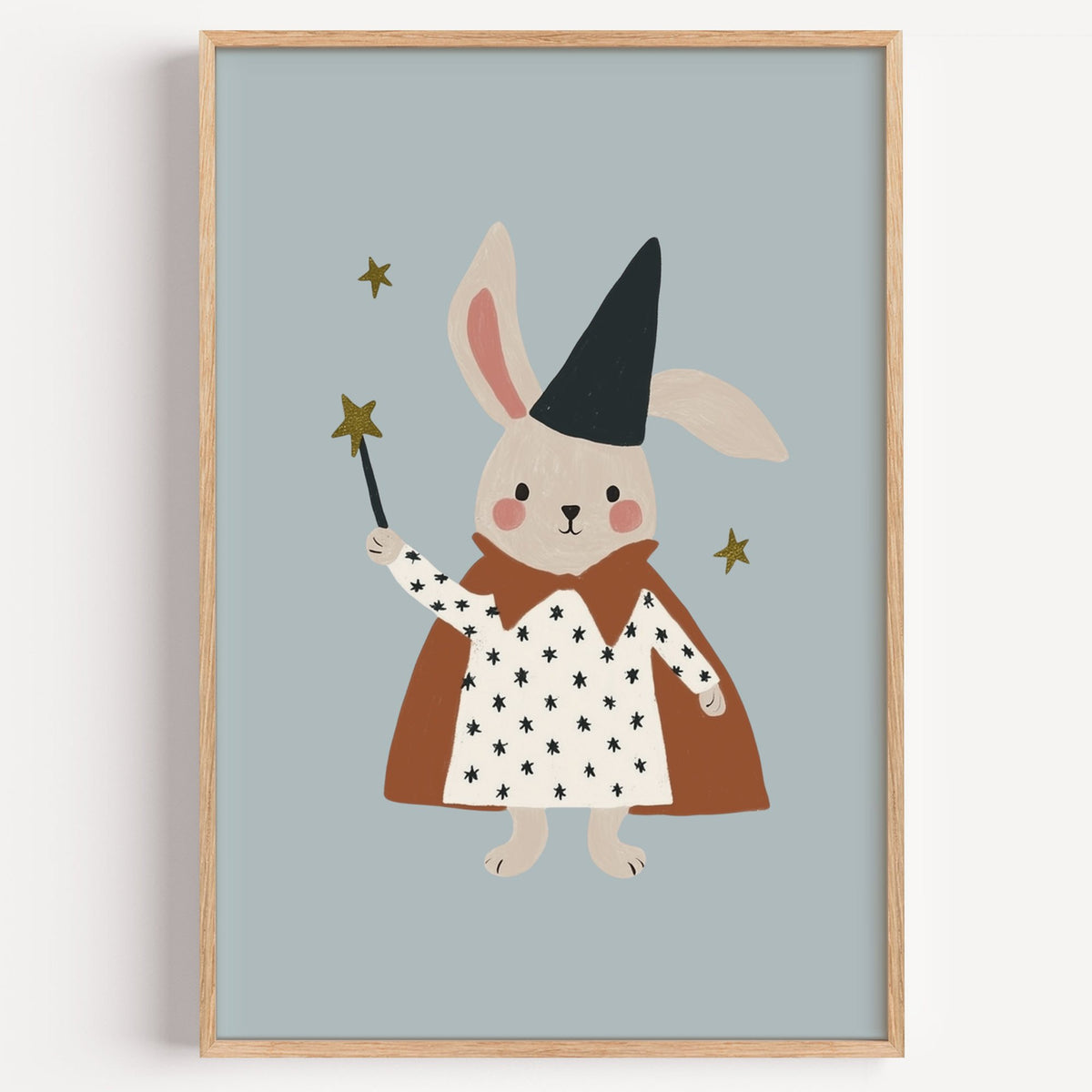Bunny magician star wand nursery print in a light oak frame on a plain white wall