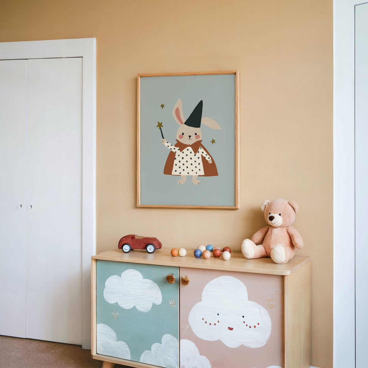 Bunny magician star wand nursery print in an oak frame on a peach wall above a cloud-painted cabinet