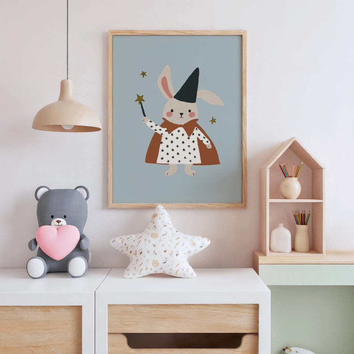 Bunny magician star wand nursery print in an oak frame above a white dresser with a star pillow and house shelf
