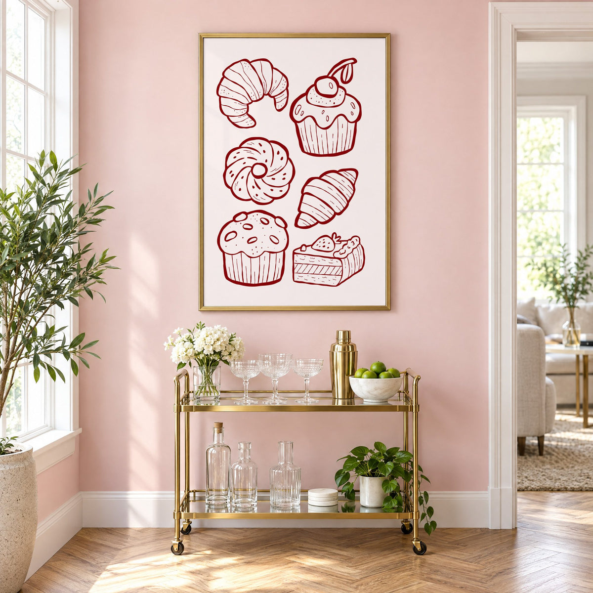 Burgundy line croissants and cupcake pastries print in a brass frame on a blush pink wall above a gold bar cart with glassware