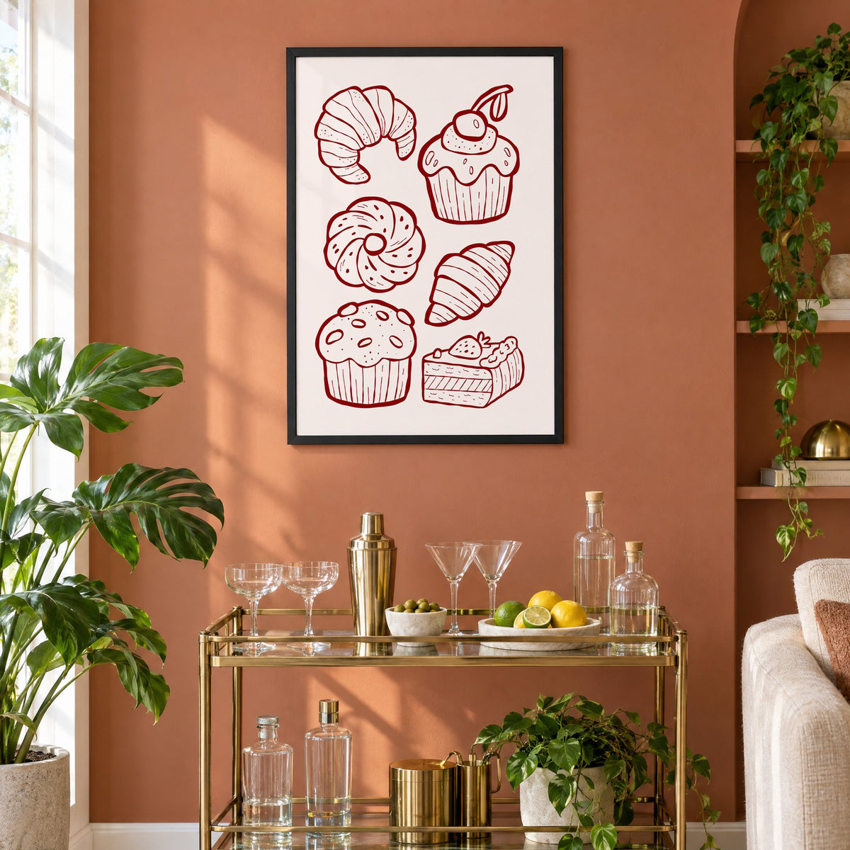 Burgundy line croissants and cupcake pastries print in a black frame on a terracotta wall above a brass bar cart with coupes and citrus
