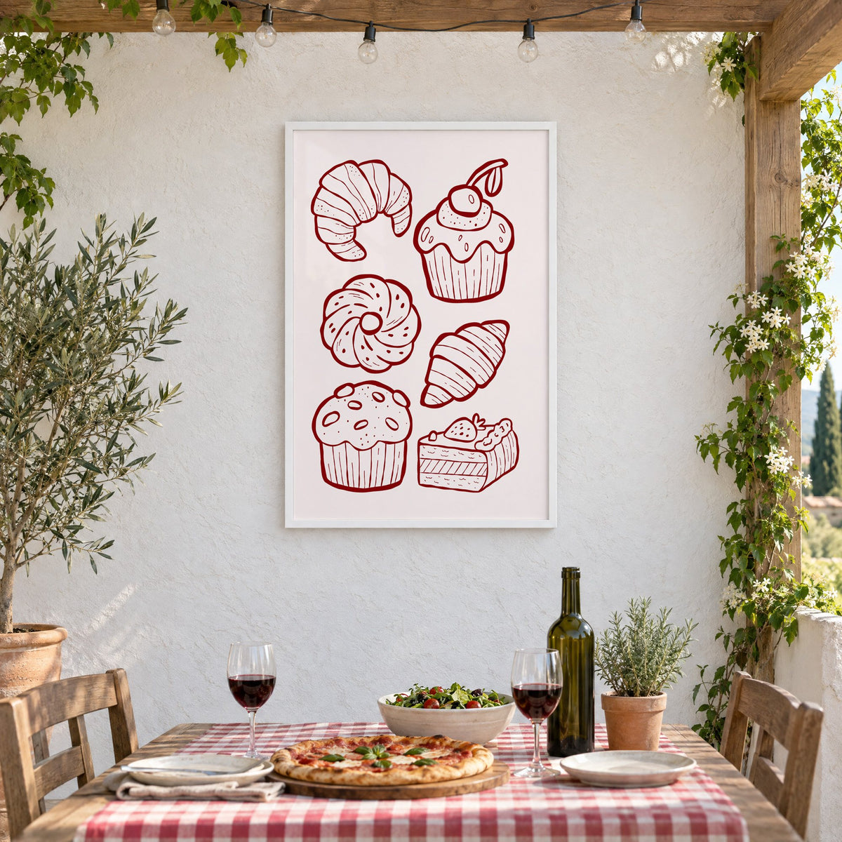 Burgundy line croissants and cupcake pastries print in a white frame on a stucco wall above a checked-cloth table with pizza and red wine