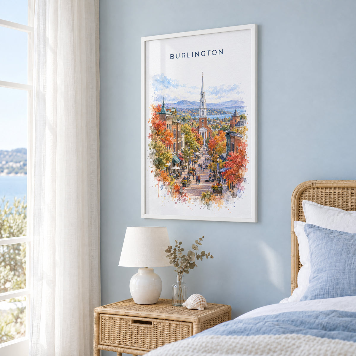 Burlington, Vermont watercolor print in a white frame on a pale blue wall beside a rattan bed in a coastal bedroom