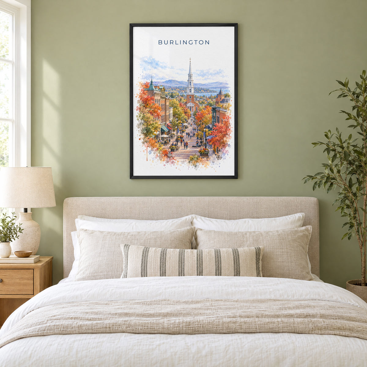 Burlington, Vermont watercolor print in a black frame above an upholstered headboard in a sage green bedroom