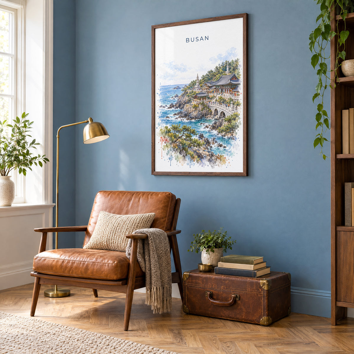 Busan watercolor print in a walnut frame on a blue wall above a leather armchair in a reading nook