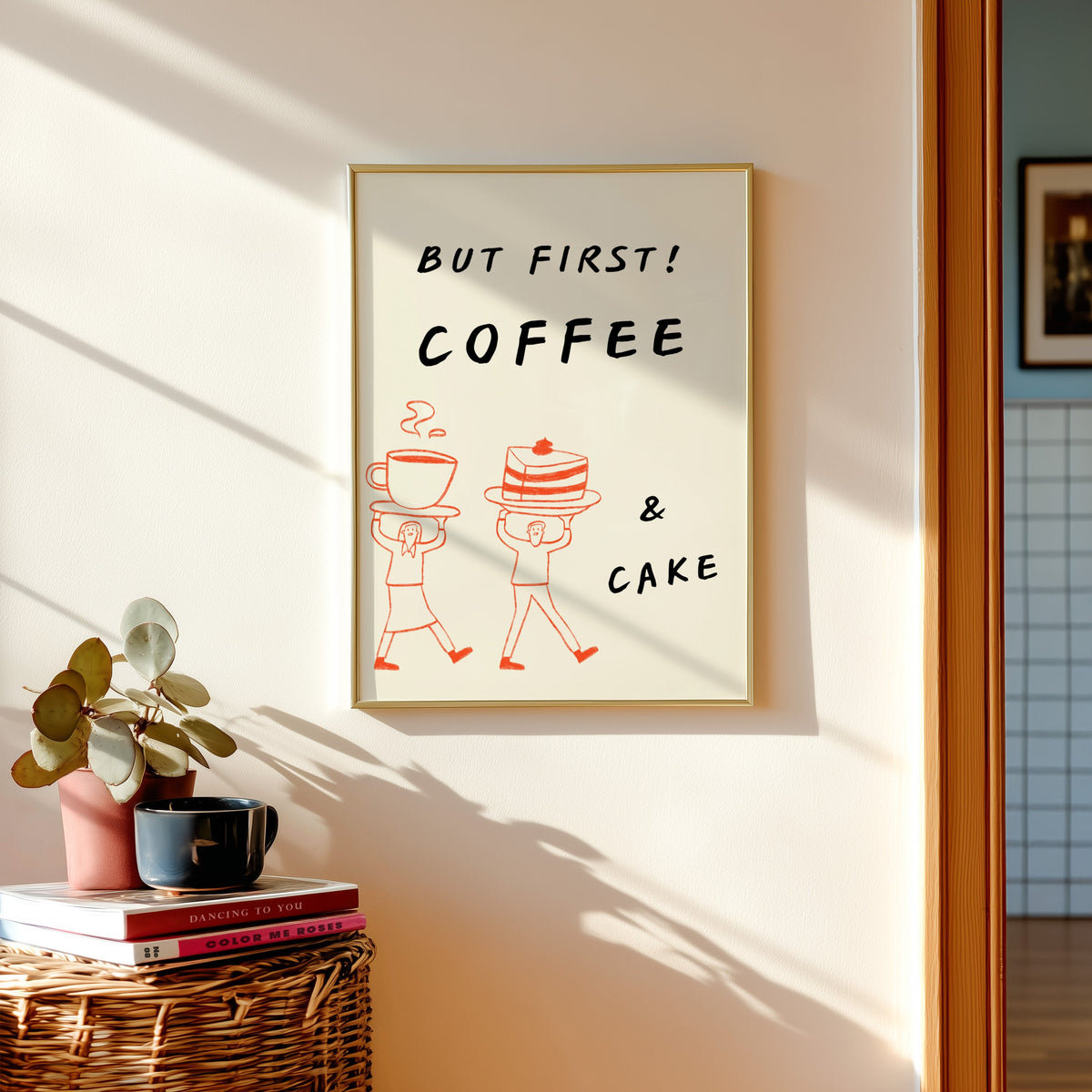 But First Coffee and Cake print shown in a gold frame above a basket of books and a pilea plant