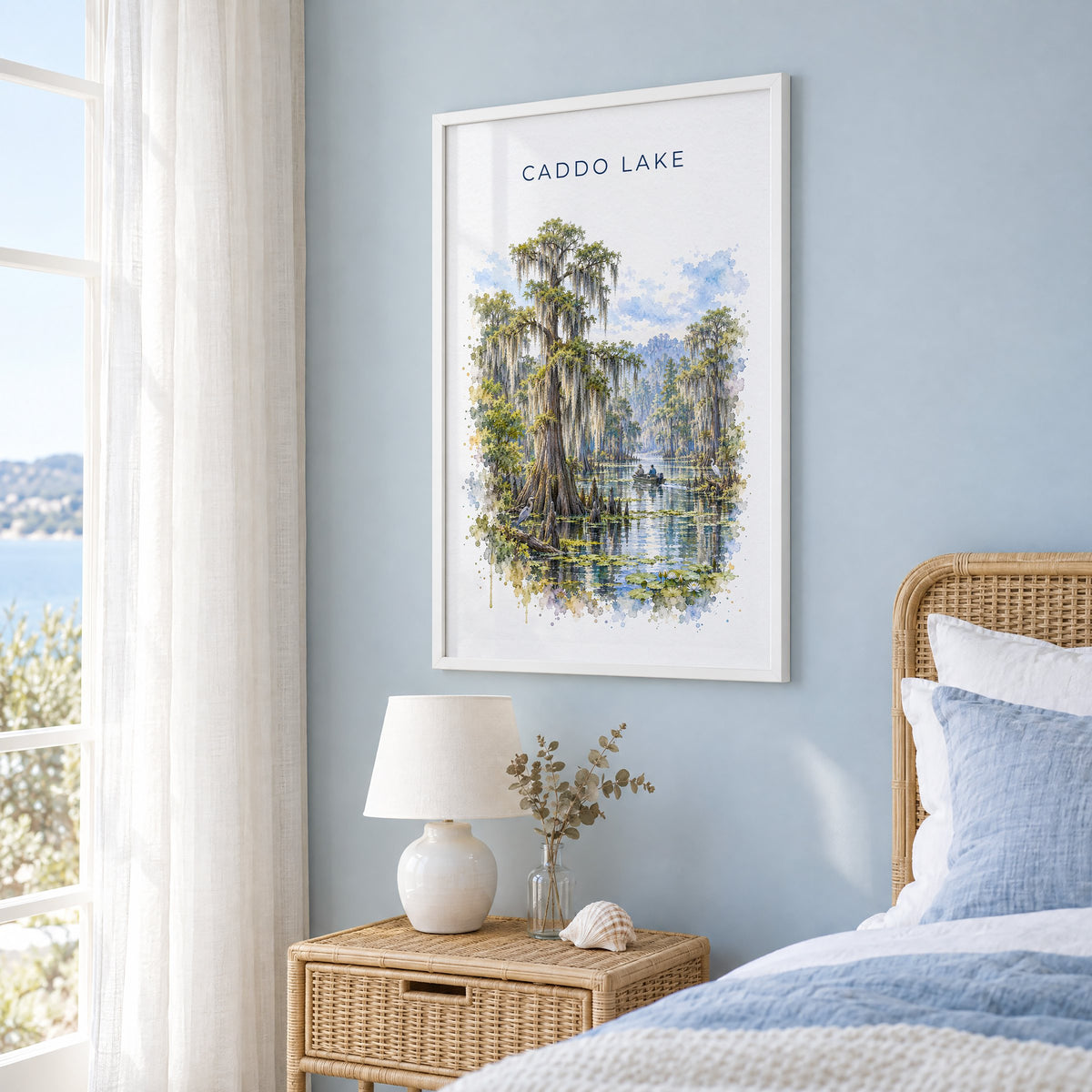 Caddo Lake watercolor print in a white frame on a pale blue wall beside a rattan bed in a coastal bedroom