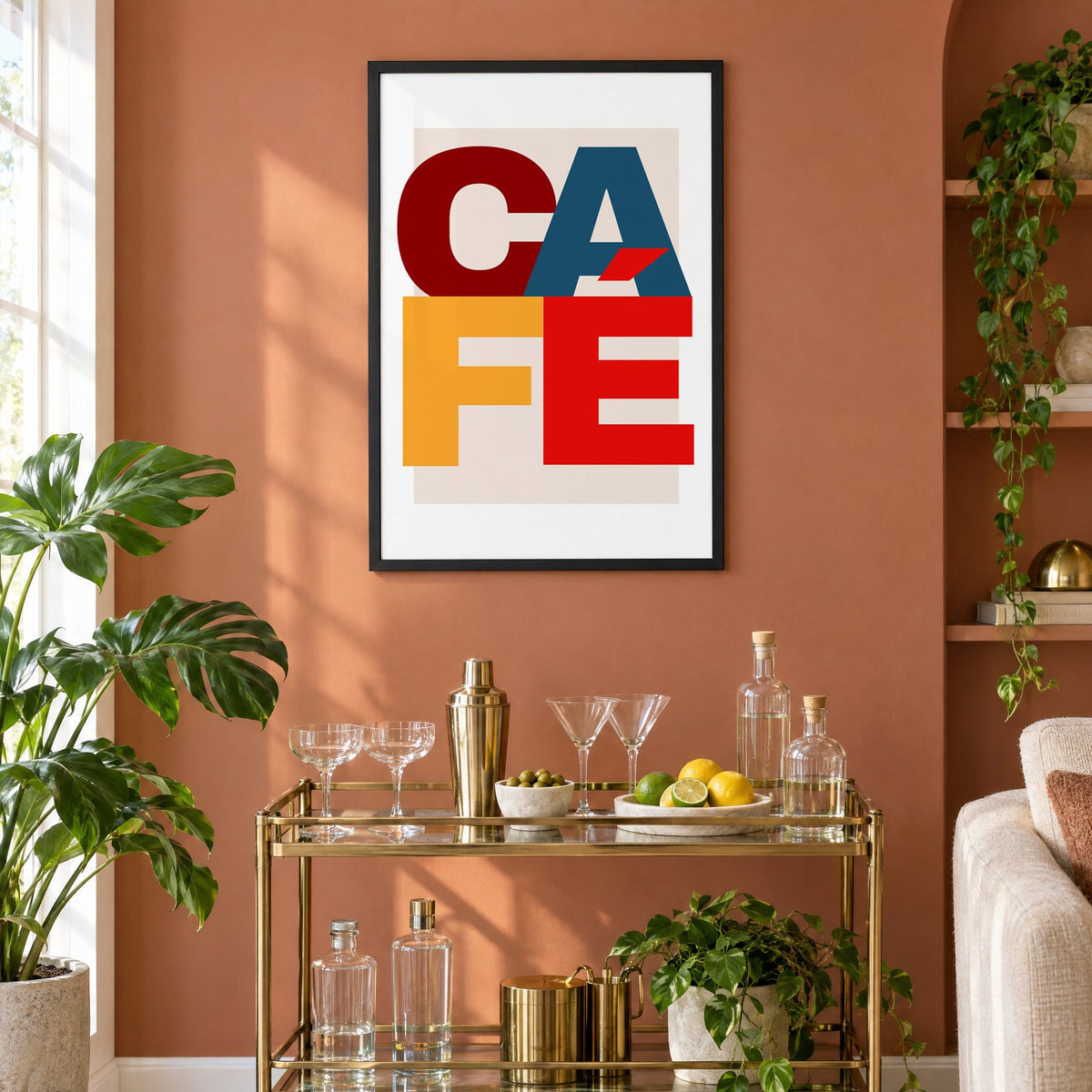 CA FÉ color block letters print in a black frame on a terracotta wall above a brass bar cart with coupes and citrus