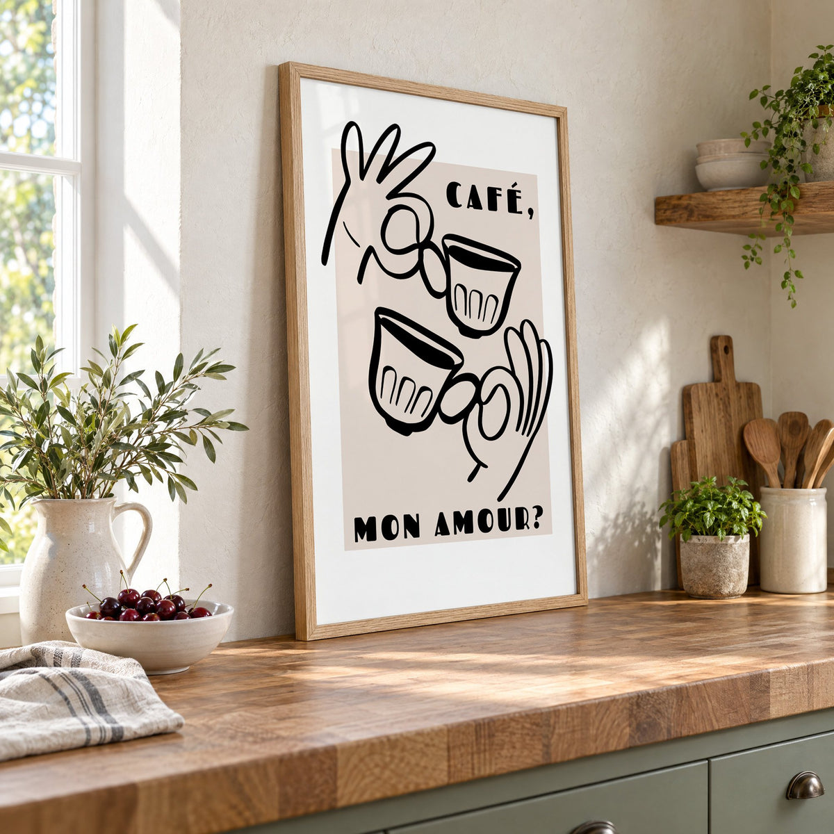 Café mon amour black line print in an oak frame leaning on a butcher block island beside a bowl of cherries