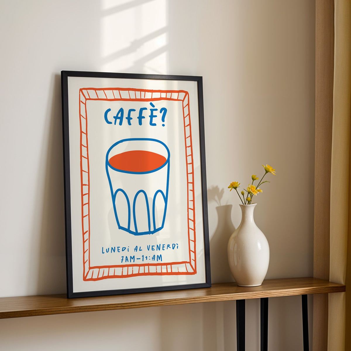 Caffe cobalt glass print in a black frame on a console table with yellow daisies