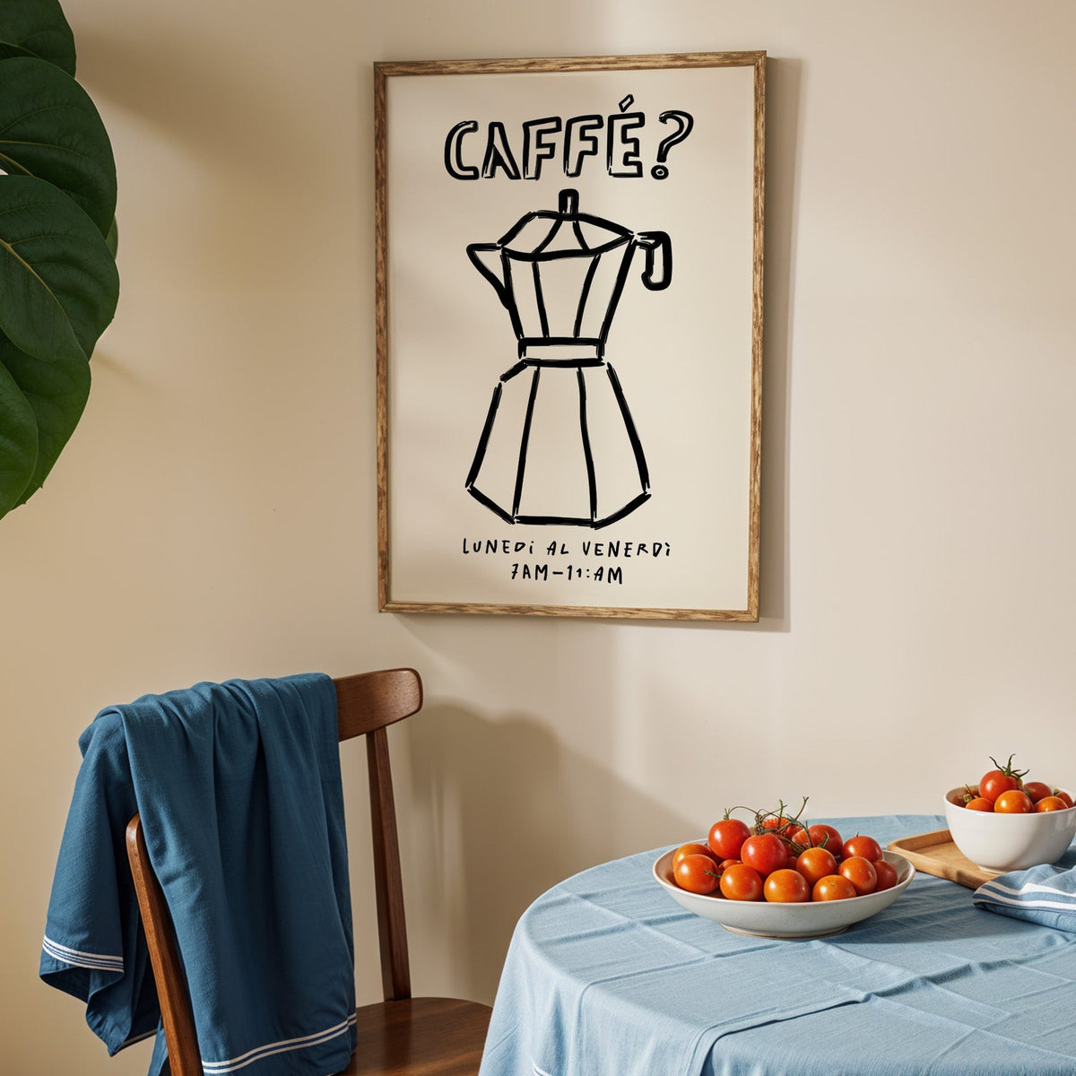 Black line moka pot print in an oak frame above a blue linen table with tomatoes