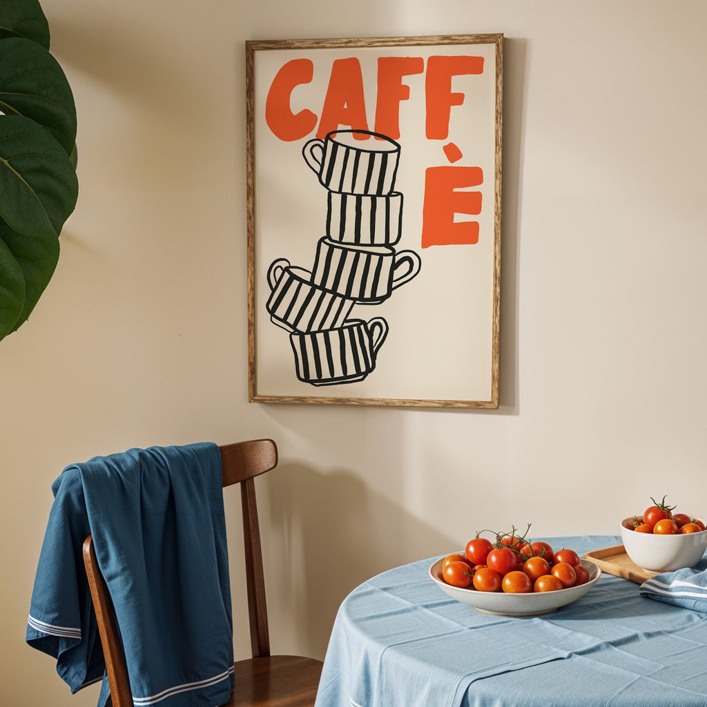 Stacked espresso cups print in an oak frame above a blue linen table with tomatoes