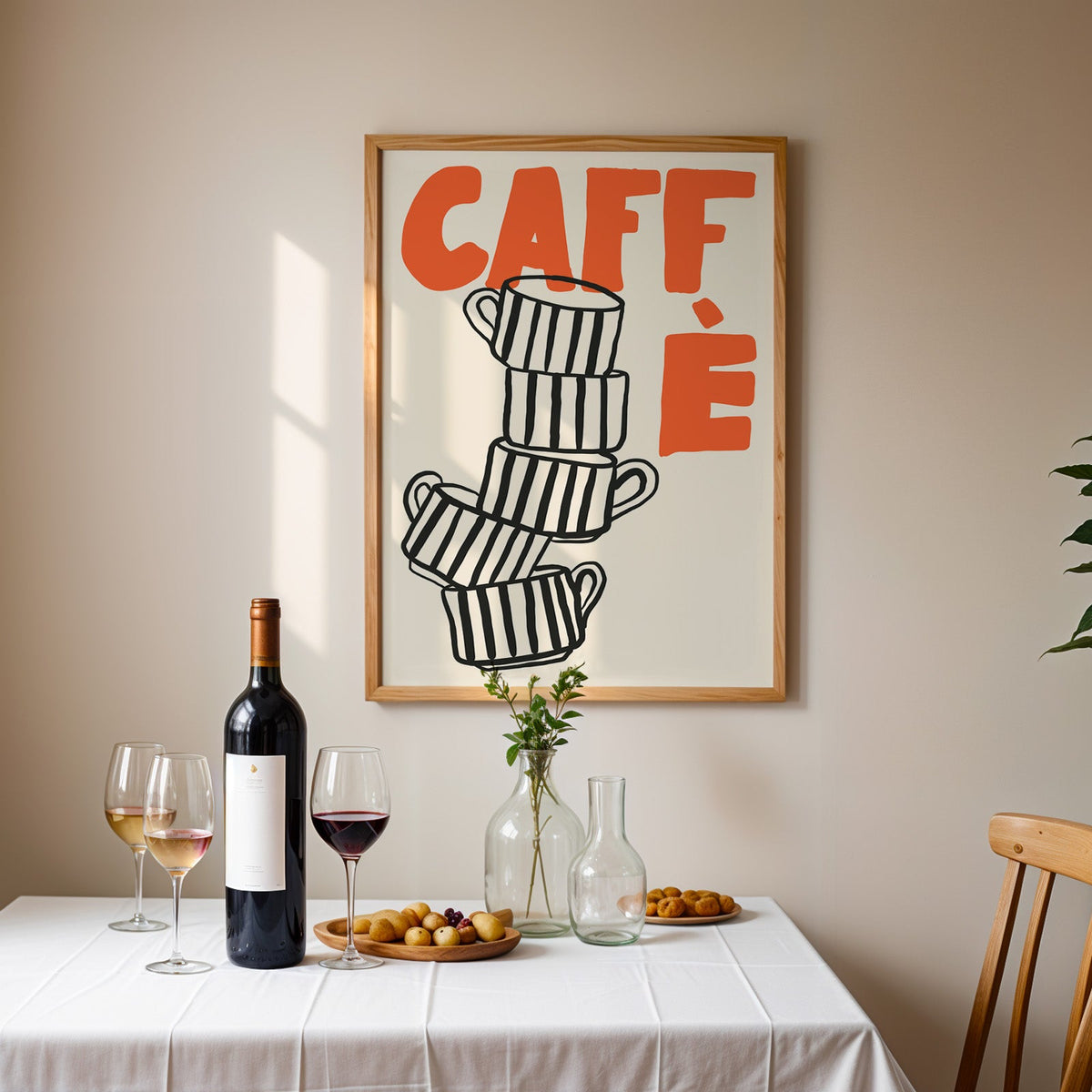 Stacked espresso cups print in an oak frame above a table laid with wine and glasses