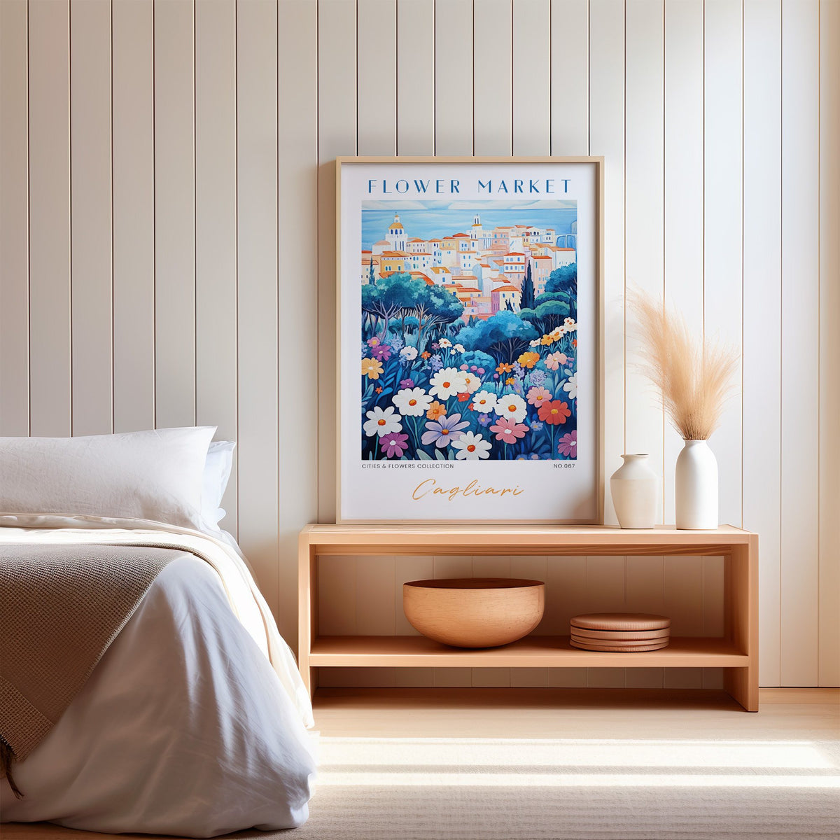 Cagliari flower market print in an oak frame on a wood bench against a white shiplap bedroom wall with pampas grass