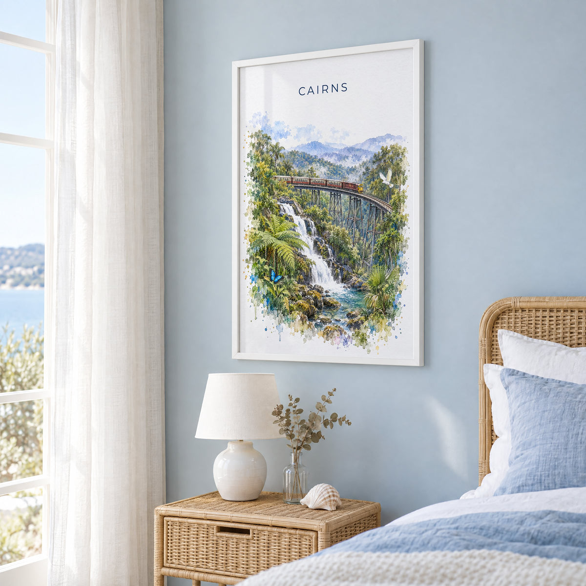 Cairns, Australia watercolor print in a white frame on a pale blue wall beside a rattan bed in a coastal bedroom
